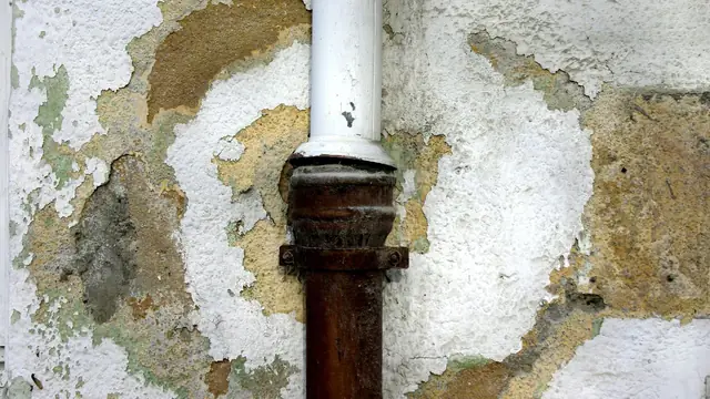 Water-damaged wall with peeling paint and plaster around a pipe