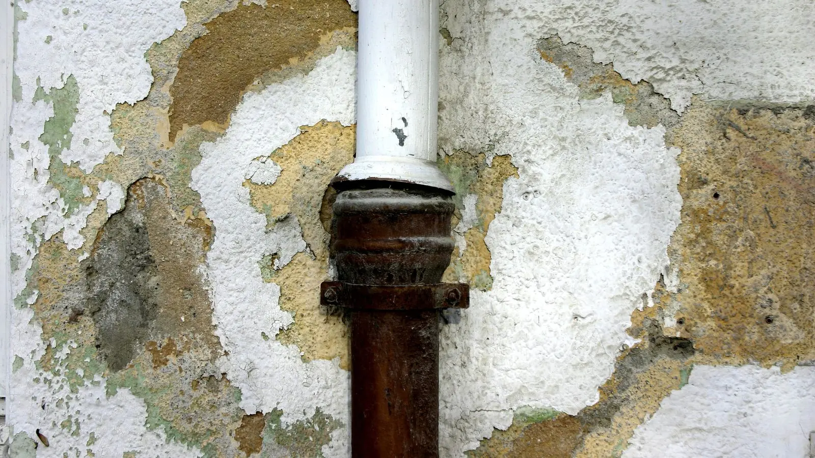 Water-damaged wall with peeling paint and plaster around a pipe